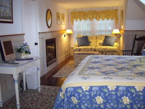 Photo of a room with king size bed dressed in a blue and yellow quit and a fireplace and sitting area in the room