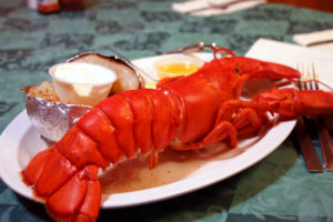 Cooked Lobster on a plate with a baked potato side-dish and melted butter