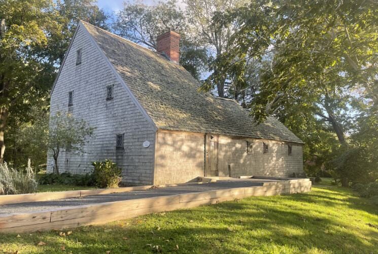 Old mill building surrounded by large green trees and green grass