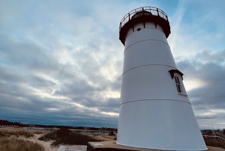Close up view of white lighthouse with a sky full of clouds in the background