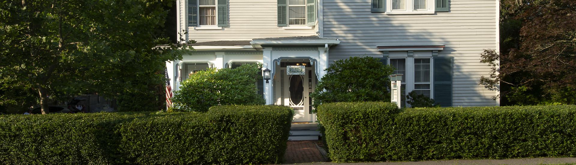 Exterior view of property painted light blue with white trim surrounded by green bushes and shrubs