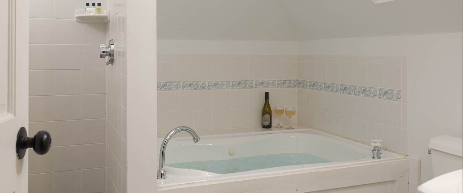 Bathroom with white walls, white tiled stand up shower, and white tiled wall around large tub full of water
