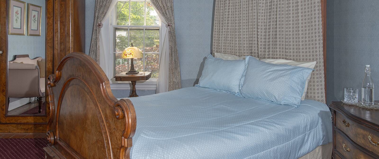 Bedroom with light blue wallpaper, carpeting, antique canopy bed, light blue bedding, and antique dark wooden hutch and dresser