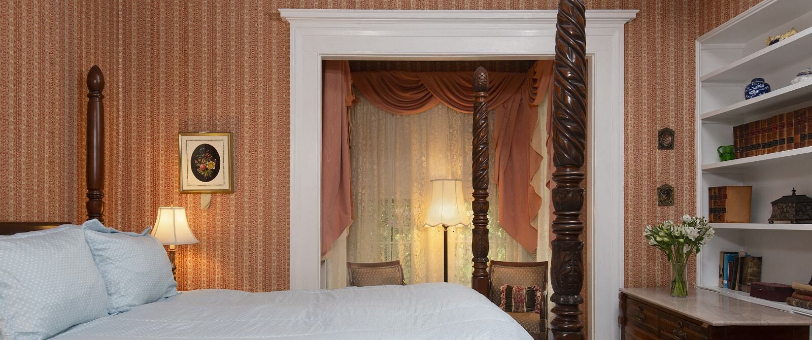 Bedroom with striped looking wallpaper, white trim, four-poster wooden bed, and dark wooden dresser