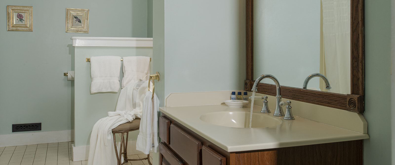 Bathroom with light green walls, light tiled floor, dark wooden vanity with cream counter, and large wooden framed mirror
