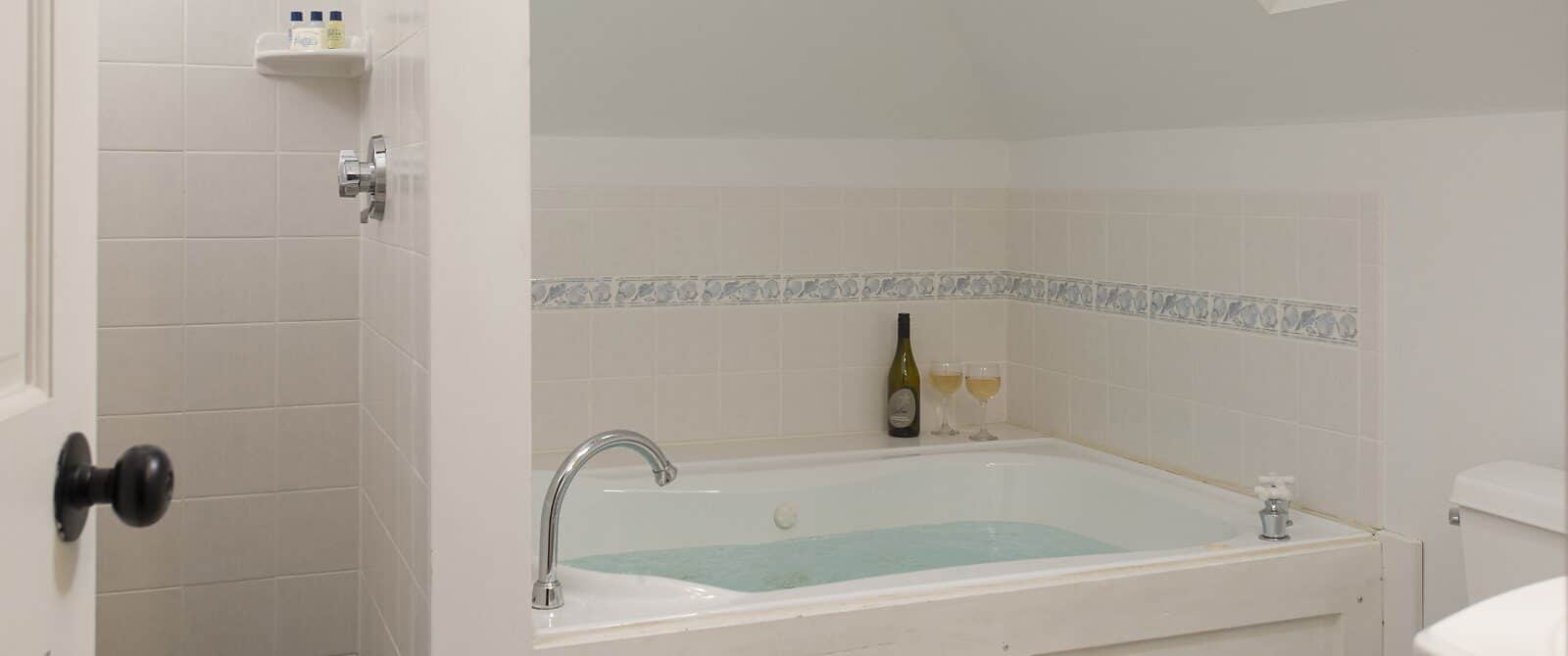 Bathroom with white walls, white tiled stand up shower, and white tiled wall around large tub full of water