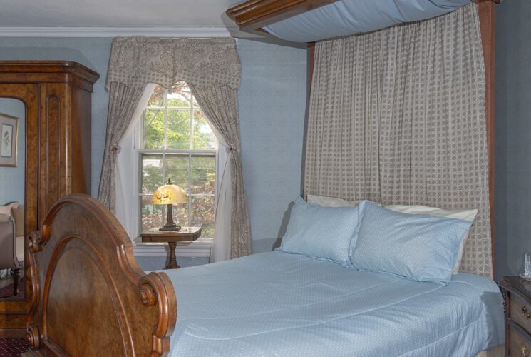 Bedroom with light blue wallpaper, carpeting, antique canopy bed, light blue bedding, and antique dark wooden hutch and dresser