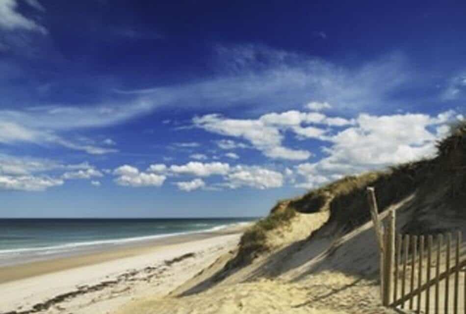 Beach with light colored sand, soft waves, and blue sky with white clouds
