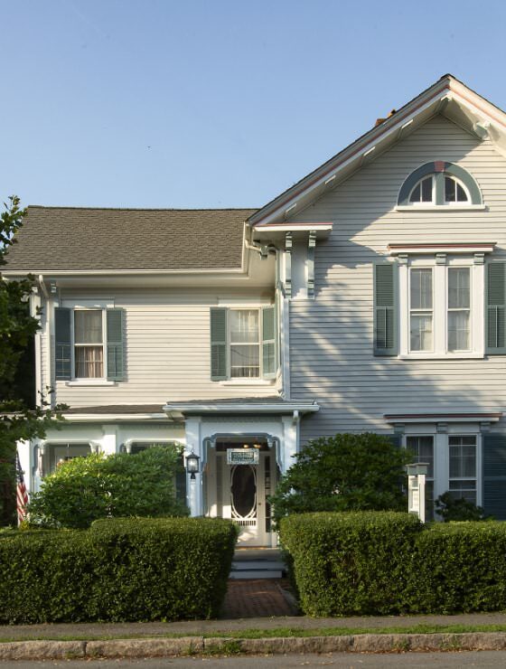 Exterior view of property painted light blue with white trim surrounded by green bushes and shrubs