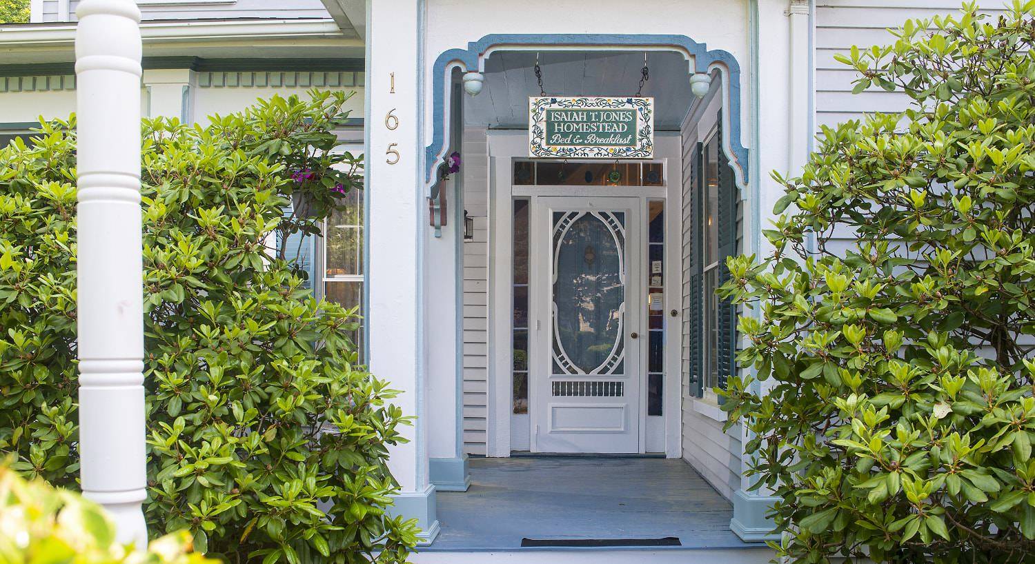 Front entry of property painted light blue with white trim surrounded by green bushes